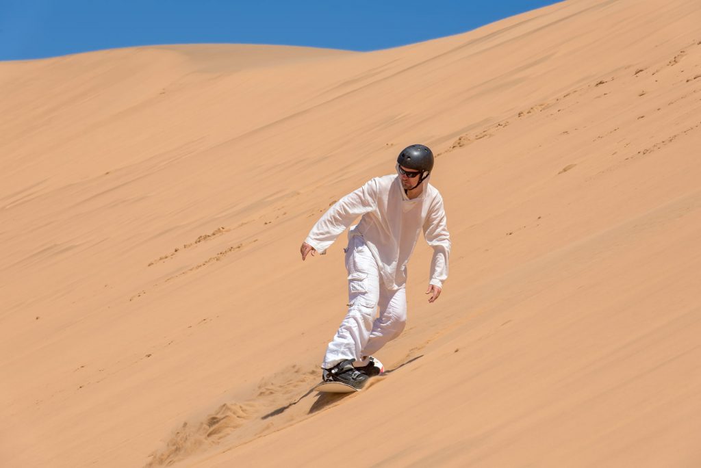 A person riding a snowboard down a sandy hill